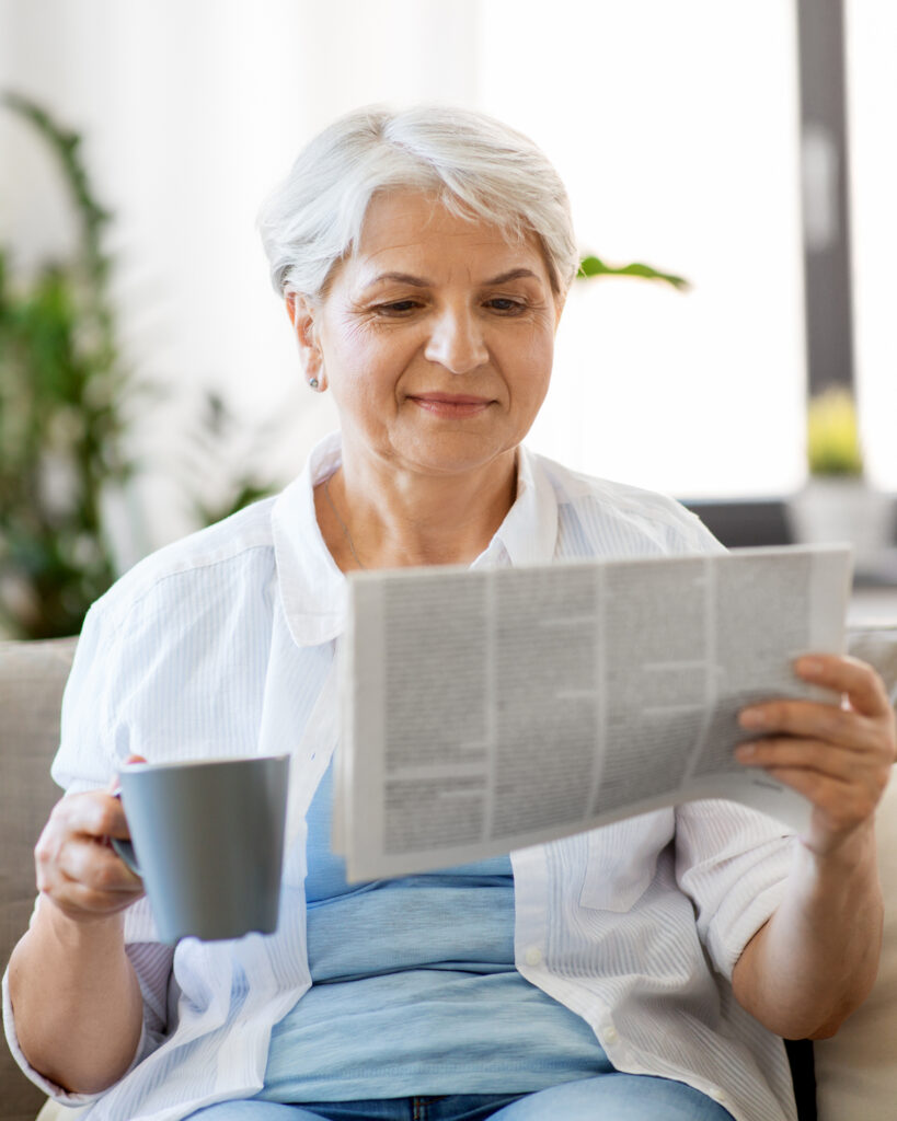 senior woman with coffee reading newspaper at home